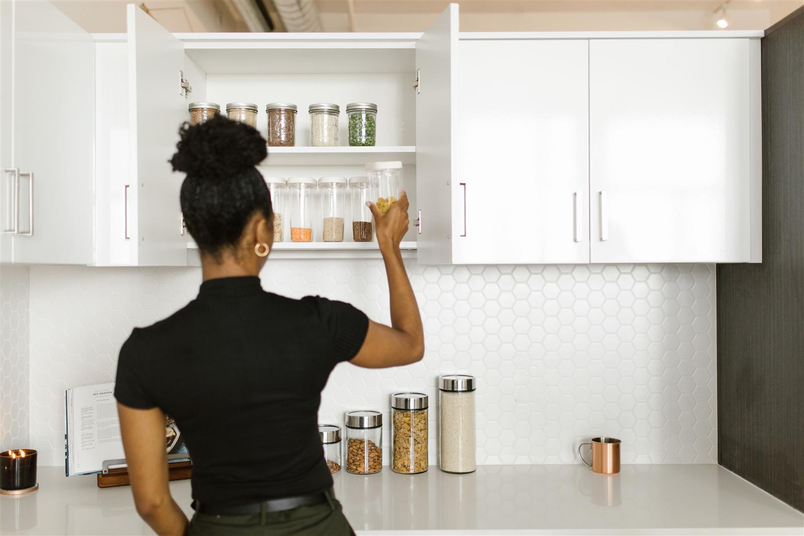 Woman organizing glass storage containers inside a kitchen cabinet