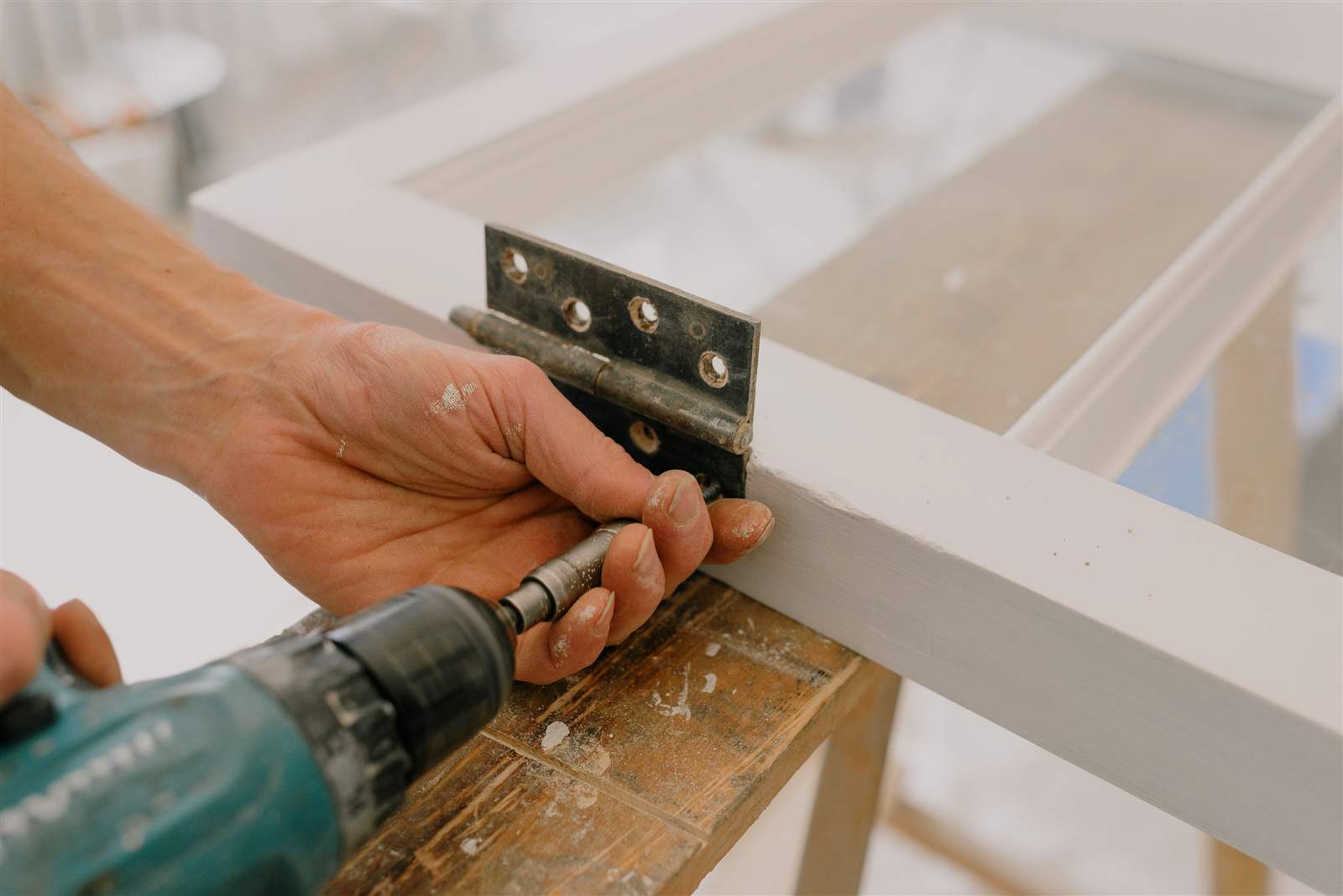 Hands using a drill-driver to tighten a hinge onto a wood frame, illustrating cabinet hinge repair